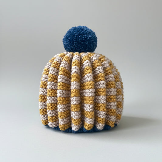 knitted tea cosy, mustard and oatmeal check with blue pompom on white bsckground
