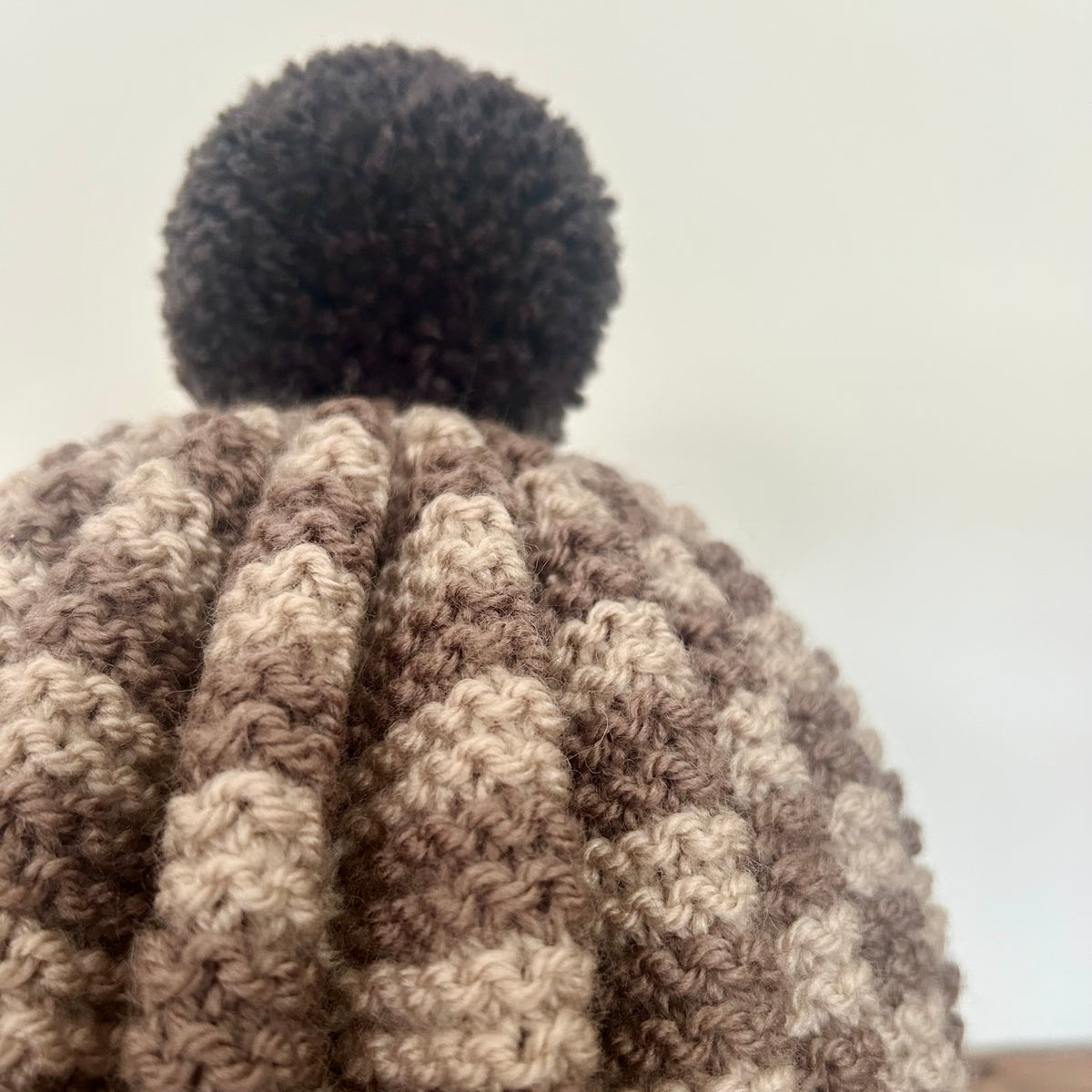 A close up of a hand knitted tea cosy with pom pom