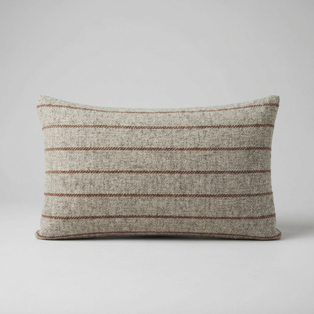 A rectangular cushion in a woven beige fabric with thin horizontal rust stripes, resting on a surface against a plain white wall.